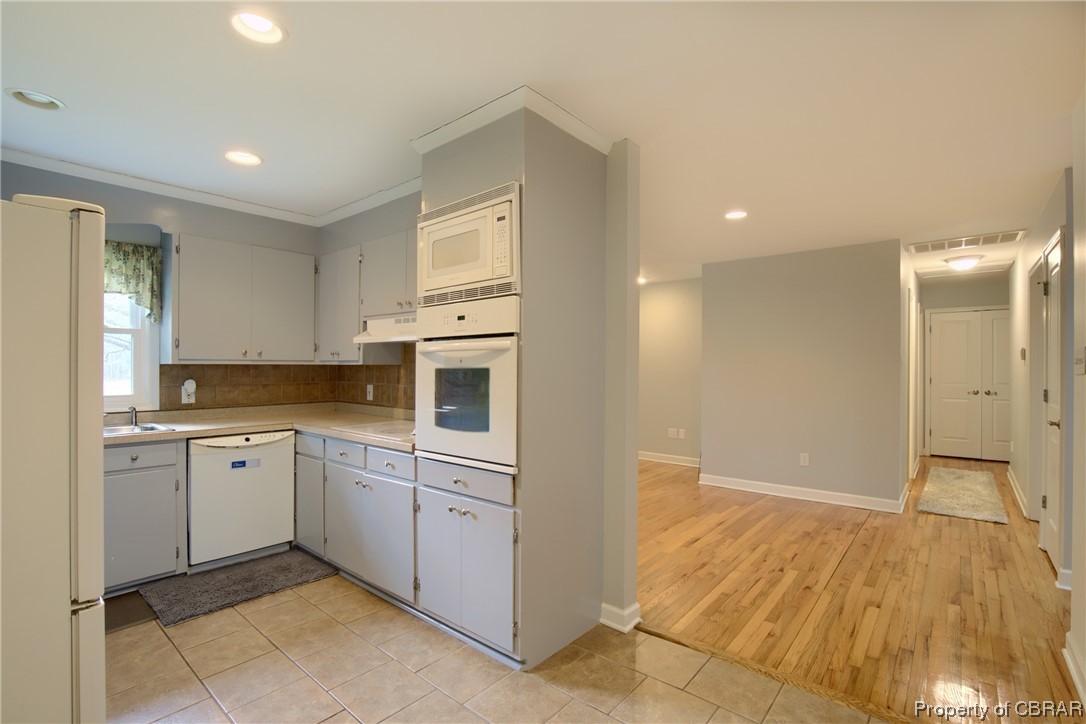 1373 Fitchetts Wharf Road Moon, VA 23119 - Photo 10 of 22 Kitchen with tasteful backsplash, white appliances, custom exhaust hood, light tile floors, and white cabinets