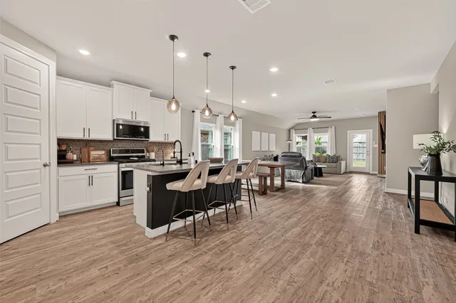 a kitchen with stainless steel appliances granite countertop a stove a sink a refrigerator a dining table and chairs with wooden floor