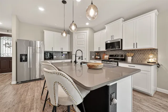 a open kitchen with stainless steel appliances granite countertop a stove a refrigerator a sink dishwasher a dining table and chairs with wooden floor