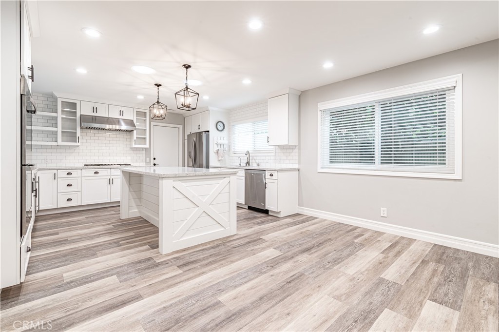 4580 Hazelnut Avenue Seal Beach, CA 90740 - Photo 12 of 34 a large white kitchen with kitchen island a stove a sink dishwasher and a fireplace with wooden floor