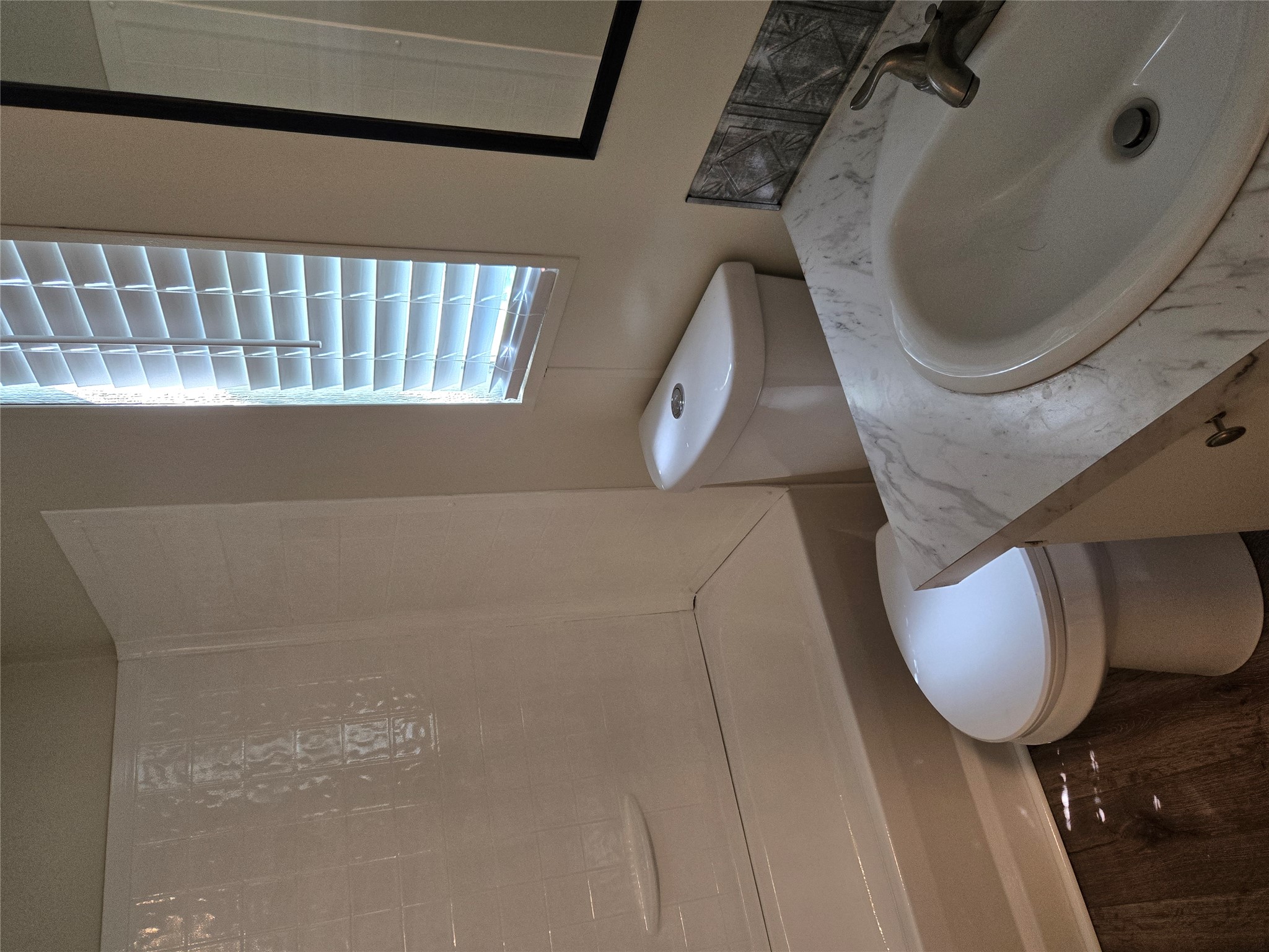 2807 Lone Tree Road Victoria, TX 77901 - Photo 7 of 12 Bathroom featuring a white bathtub and shower surround, a window with horizontal blinds, wood-finish flooring, a white vanity with an integrated sink, and a framed mirror