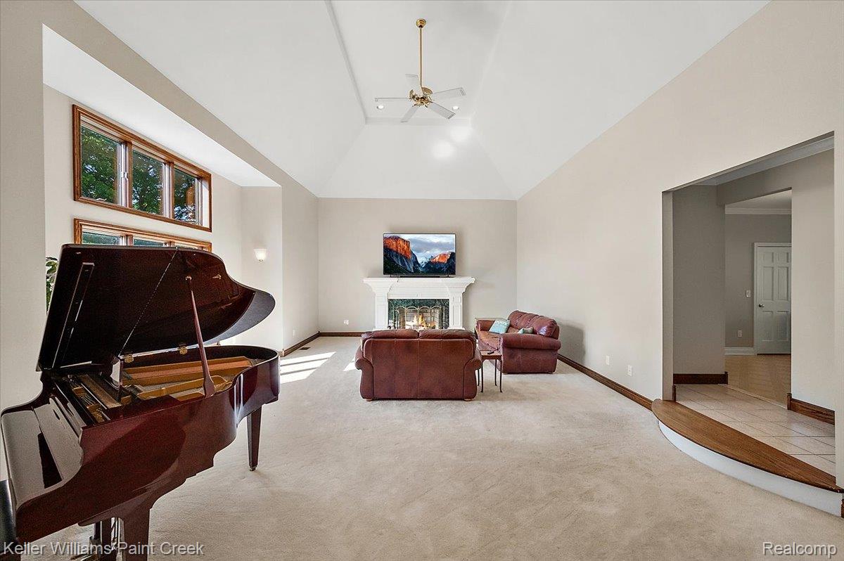 69069 Campground Road Romeo, MI 48065 - Photo 21 of 78 Spacious living area featuring a vaulted ceiling with a central fan, light-toned carpeting, and a fireplace with a white mantel