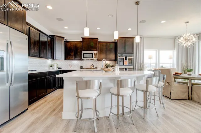 a kitchen with stainless steel appliances kitchen island granite countertop a stove a sink a refrigerator a dining table and chairs with wooden floor