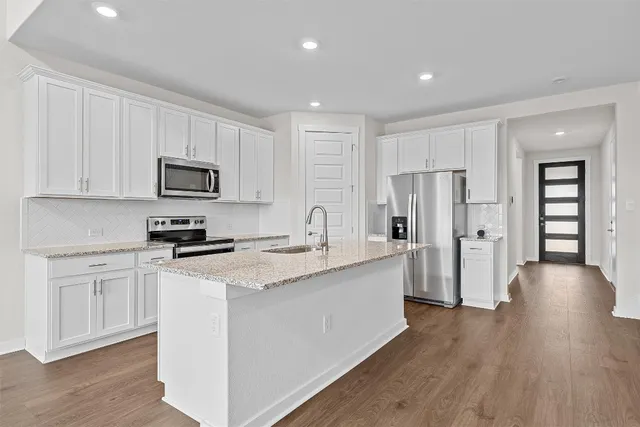 a kitchen with stainless steel appliances granite countertop a refrigerator a stove top oven a sink and white cabinets with wooden floor