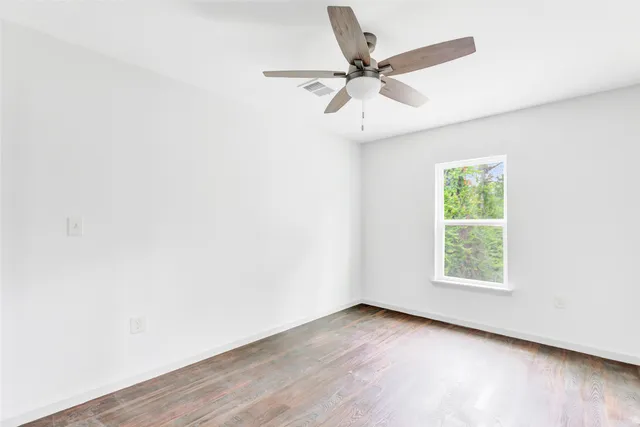 an empty room with wooden floor window and ceiling fan