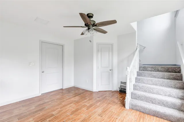 a view of an empty room with wooden floor and a ceiling fan