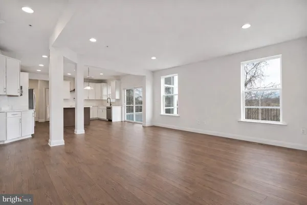 a view of an empty room with wooden floor and a kitchen