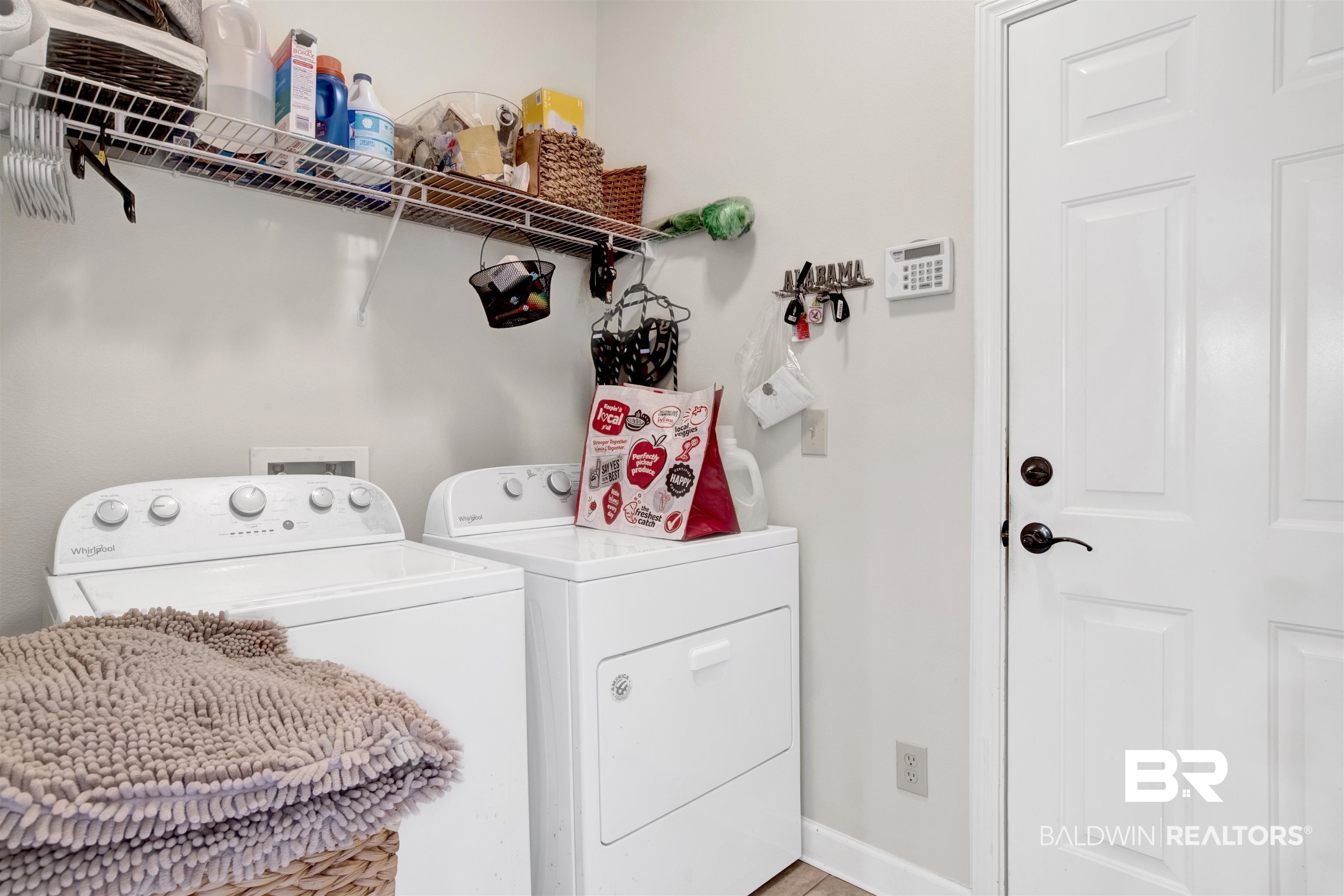 10368 Gayfer Rd Extension Fairhope, AL 36532 - Photo 29 of 43 Dedicated utility area featuring a washer and dryer, an overhead wire shelving unit, and a paneled door with dark hardware