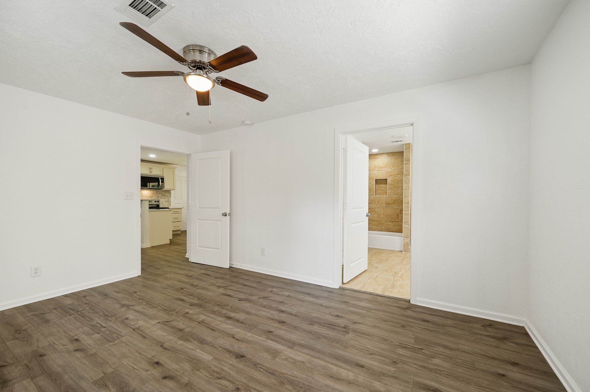 61 Hicks Loop West Cleveland, TX 77328 - Photo 18 of 38 Spacious room with elegant wood flooring, ceiling fan, and abundant natural light, leading to a modern kitchen and a stylish bathroom with tile accents.