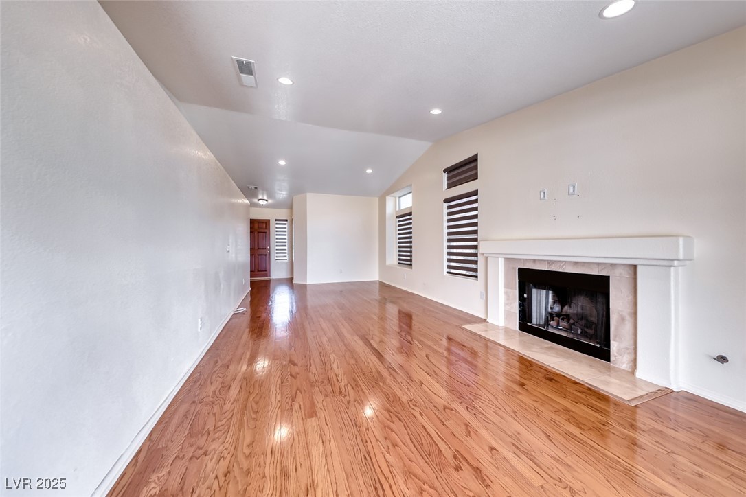 386 Nassau Way Boulder City, NV 89005 - Photo 11 of 44 Unfurnished living room featuring a tiled fireplace, light wood-type flooring, vaulted ceiling, and recessed lighting