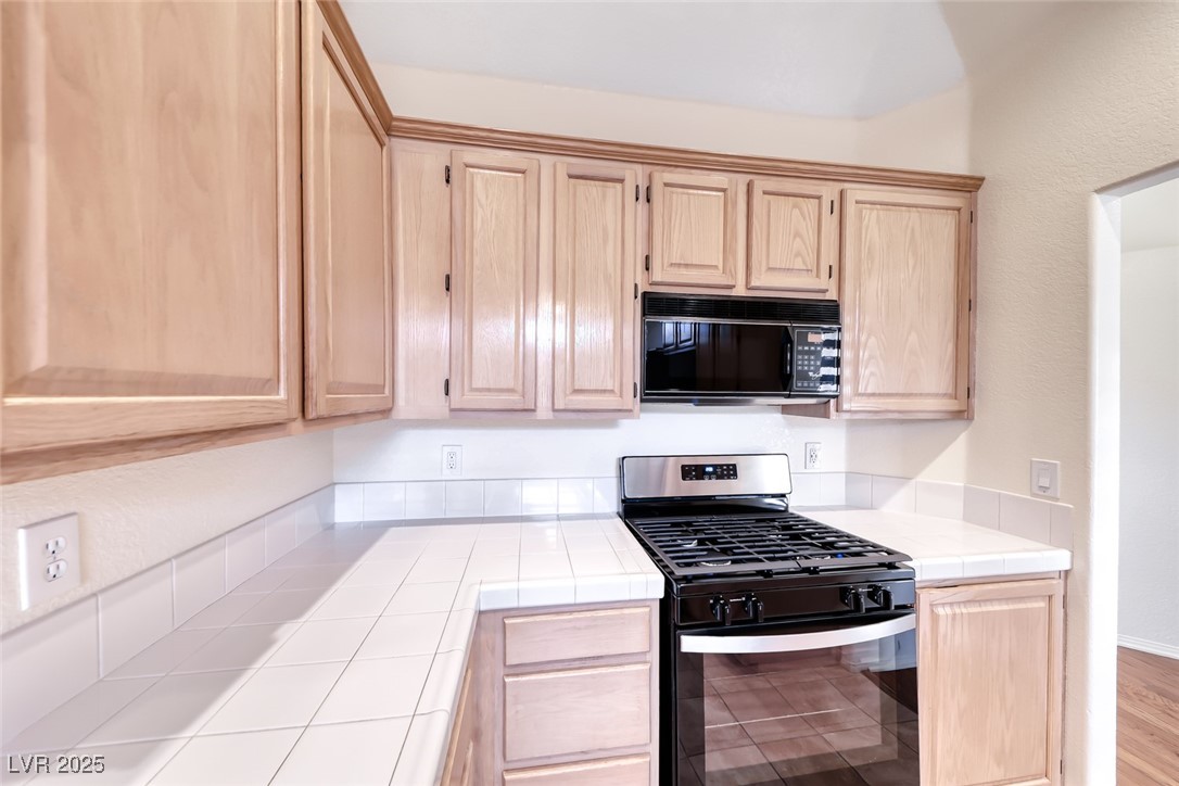386 Nassau Way Boulder City, NV 89005 - Photo 16 of 44 Kitchen featuring light brown cabinetry, gas range, black microwave, tile counters, and wood finished floors