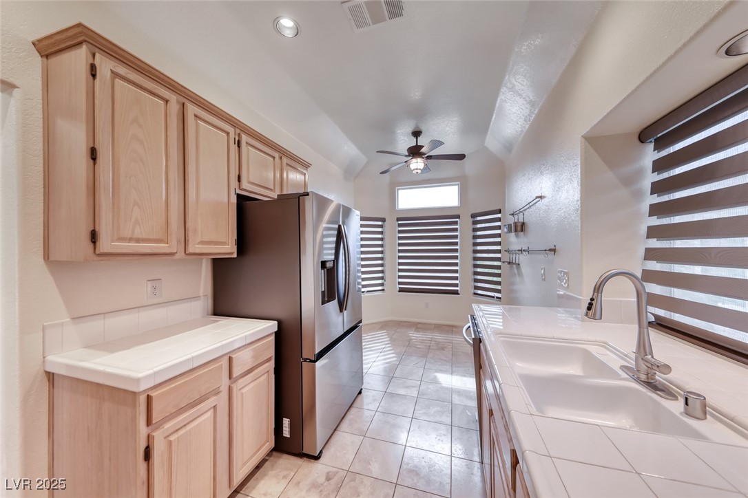 386 Nassau Way Boulder City, NV 89005 - Photo 19 of 44 Kitchen featuring tile counters, light brown cabinetry, stainless steel refrigerator with ice dispenser, a ceiling fan, and lofted ceiling