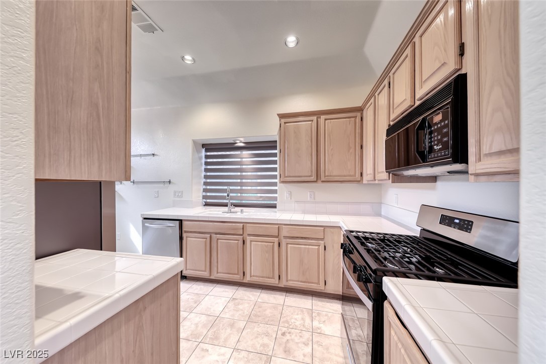 386 Nassau Way Boulder City, NV 89005 - Photo 20 of 44 Kitchen with light brown cabinets, stainless steel gas stove, tile countertops, black microwave, and recessed lighting