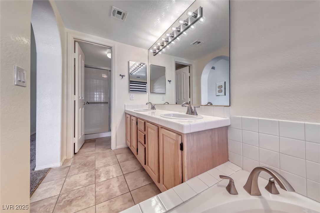 386 Nassau Way Boulder City, NV 89005 - Photo 25 of 44 Bathroom featuring a textured wall, a shower stall, double vanity, light tile patterned floors, and a bath