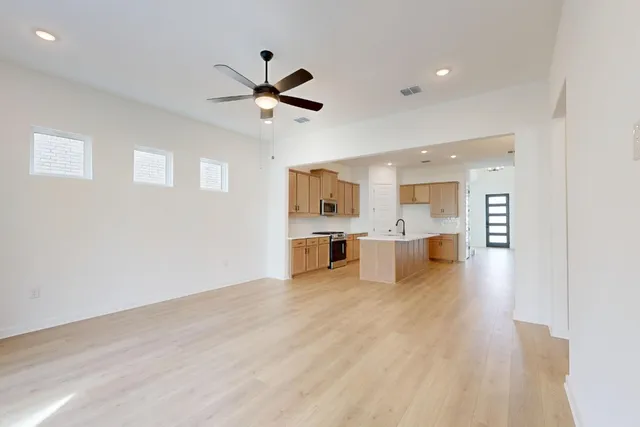 a large kitchen with stainless steel appliances granite countertop a stove a sink a refrigerator and white cabinets with wooden floor