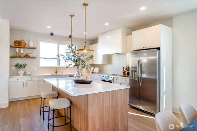 a kitchen with stainless steel appliances granite countertop a refrigerator a sink dishwasher a stove and a dining table with wooden floor