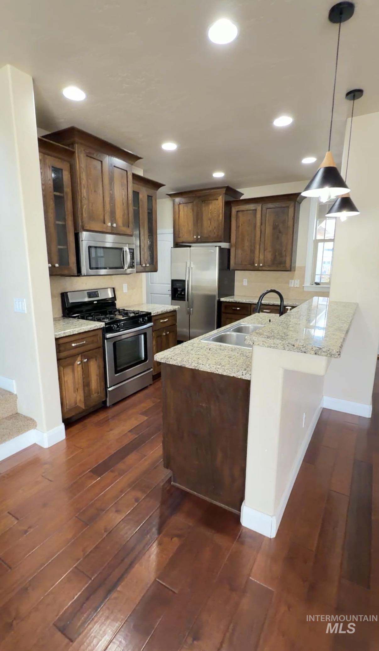 4678 North Elmstone Avenue Meridian, ID 83646 - Photo 5 of 15 Kitchen with appliances with stainless steel finishes, dark brown cabinets, a peninsula, glass insert cabinets, and hanging light fixtures