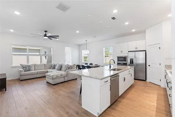 a large white kitchen with stainless steel appliances kitchen island a stove a refrigerator a couch and a view of living room