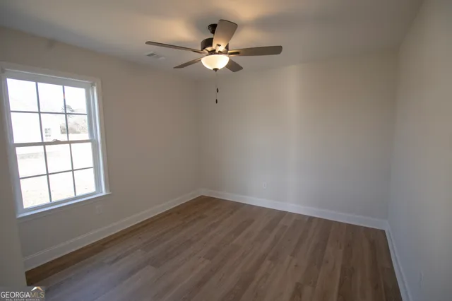 an empty room with wooden floor fan and windows