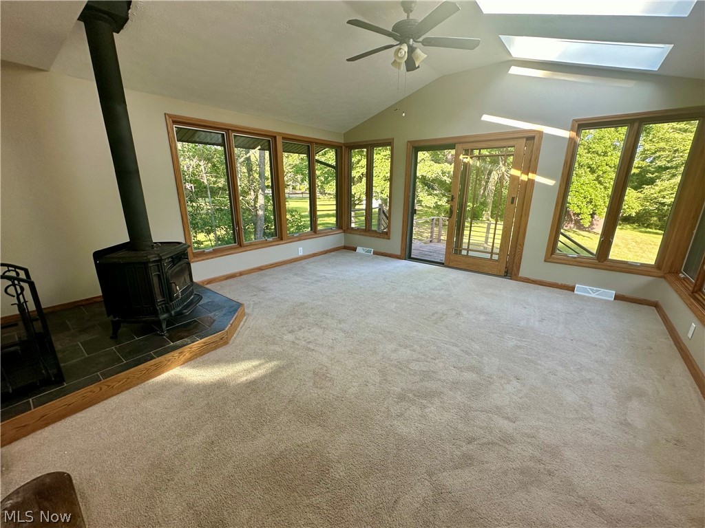 5855 Liberty Road Solon, OH 44139 - Photo 8 of 19 Unfurnished living room featuring a wood stove, a healthy amount of sunlight, vaulted ceiling with skylight, and ceiling fan
