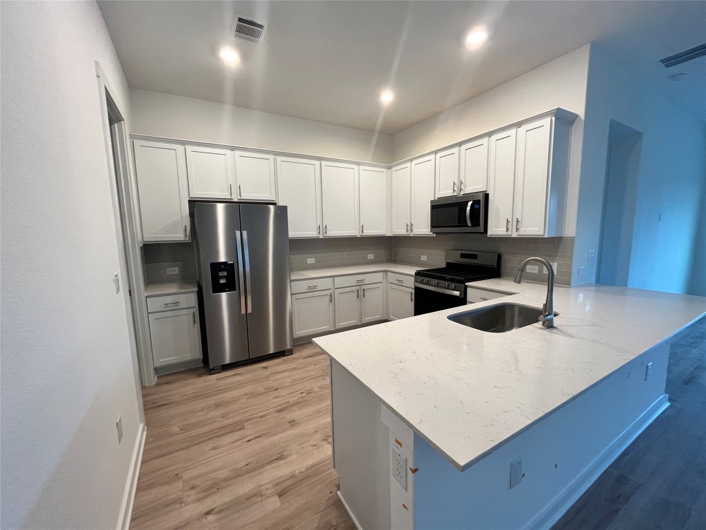 2012 Bobtail Pass Leander, TX 78641 - Photo 9 of 22 Kitchen featuring stainless steel appliances, a peninsula, white cabinets, light stone countertops, and recessed lighting