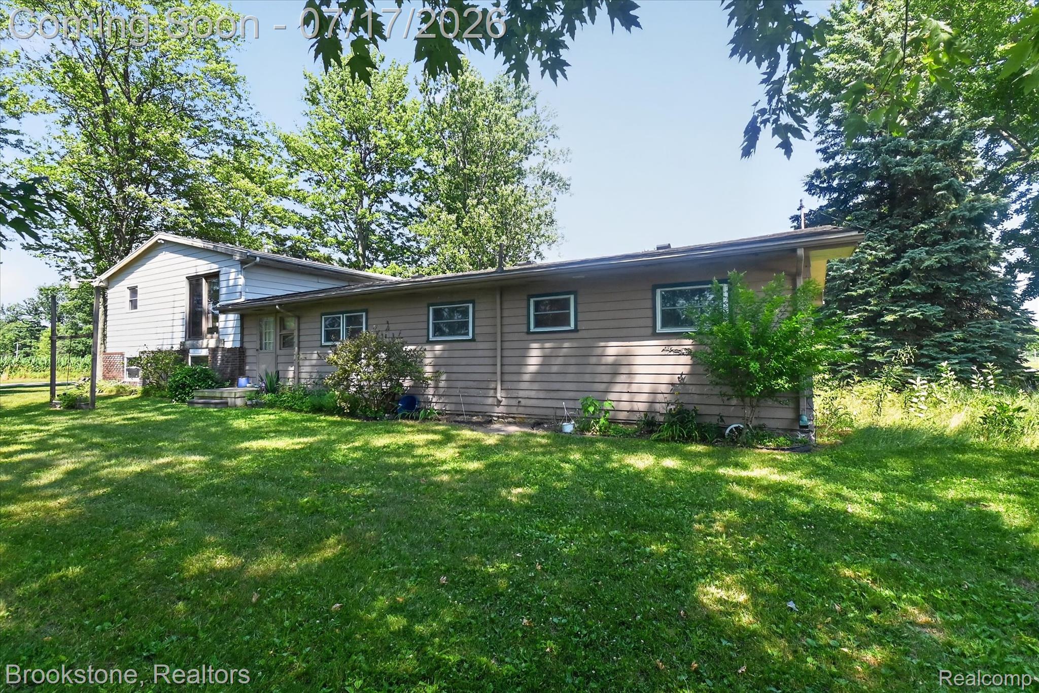 22025 Lakefield Road Merrill, MI 48637 - Photo 42 of 47 Expansive green lawn surrounds the property, featuring a multi-level structure with tan siding and a secondary light-colored siding section