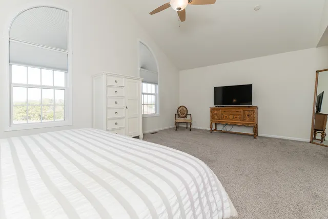 a spacious bedroom with a bed and a flat tv screen on dresser