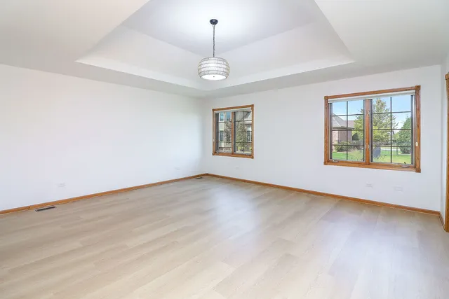 an empty room with wooden floor chandelier and windows