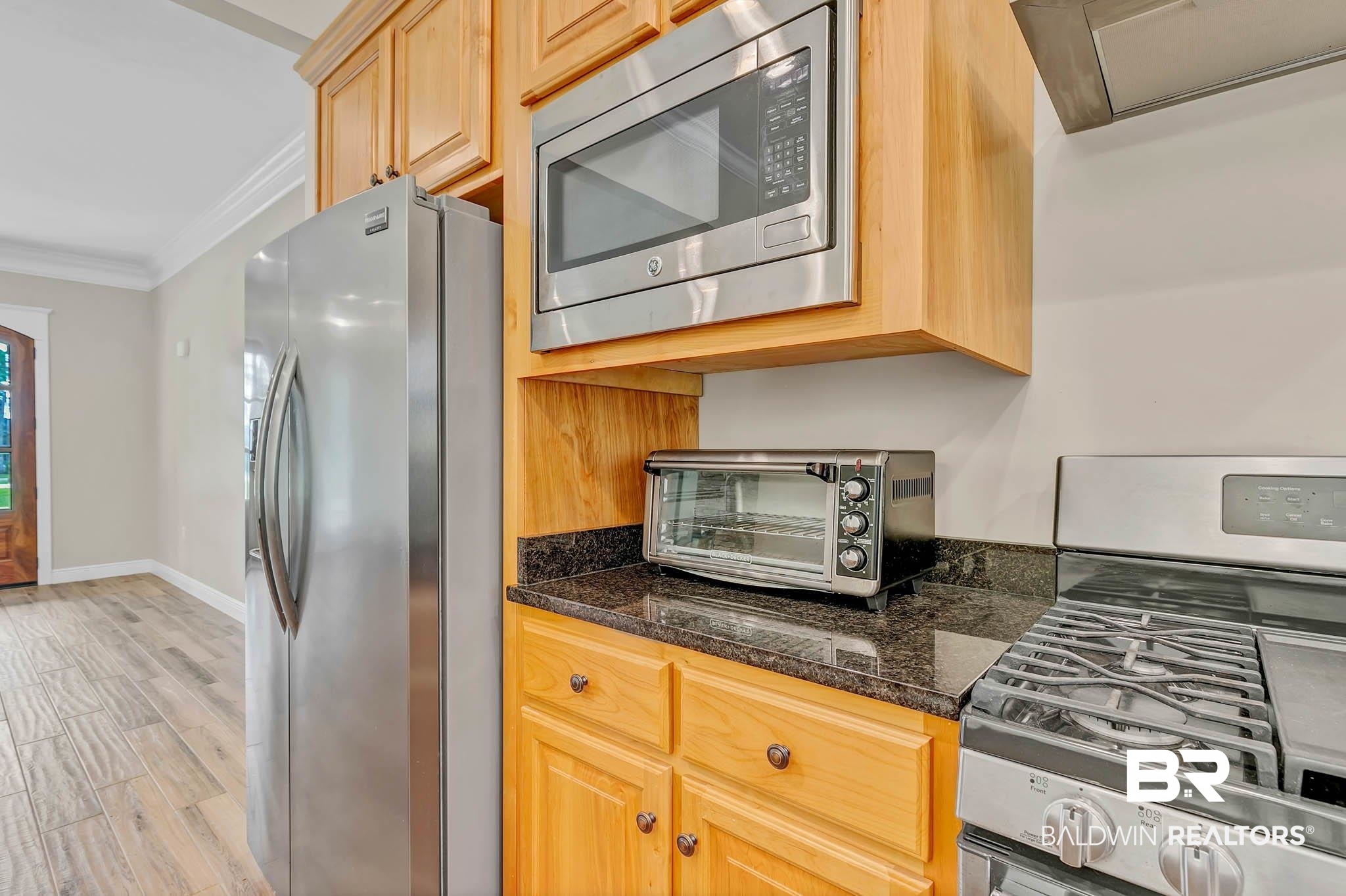 8145 Bay View Drive Foley, AL 36535 - Photo 25 of 81 Kitchen featuring appliances with stainless steel finishes, crown molding, light wood finished floors, dark stone counters, and range hood