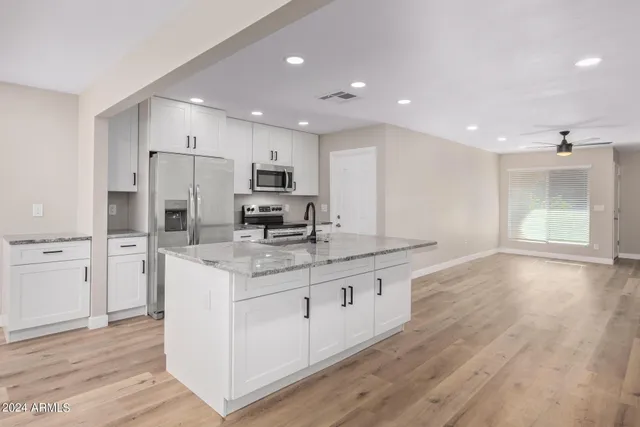 a kitchen with stainless steel appliances granite countertop a stove a sink a refrigerator and white cabinets with wooden floor