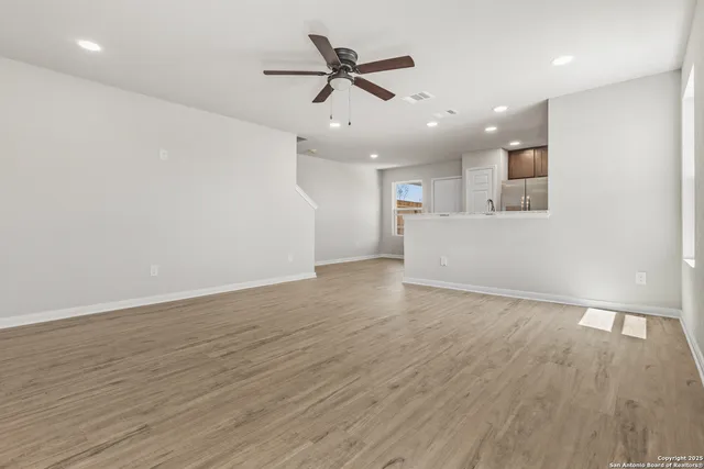 a view of an empty room with wooden floor and a ceiling fan