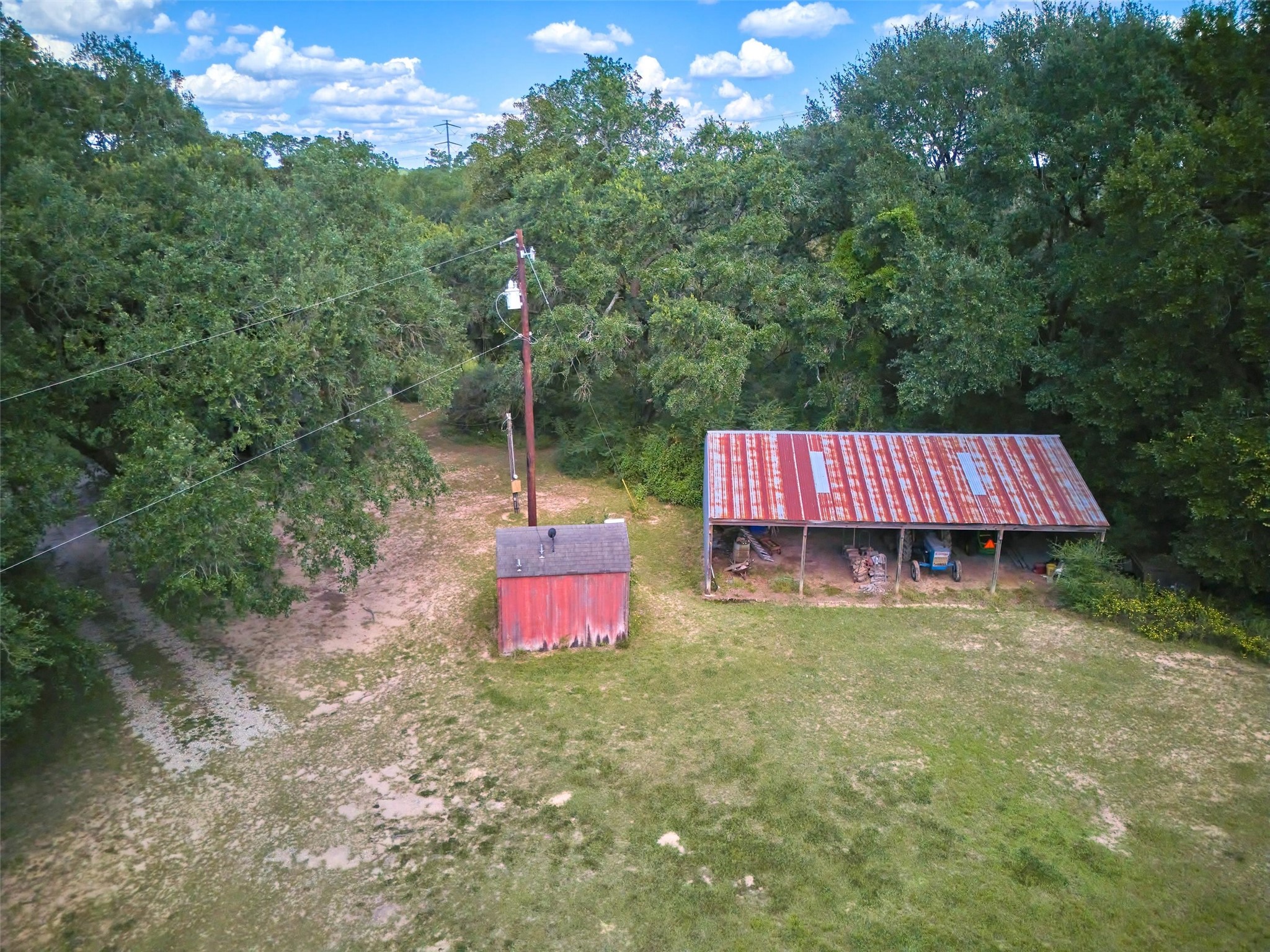 24030 Hegar Road Hockley, TX 77447 - Photo 5 of 40 This aerial view highlights the property’s functional improvements, showcasing the barn and shed perfectly positioned within the 50 acres. Surrounded by open pastures and shaded by mature trees, these structures are ideal for equipment storage, livestock, or future expansion, adding both utility and value to the land.