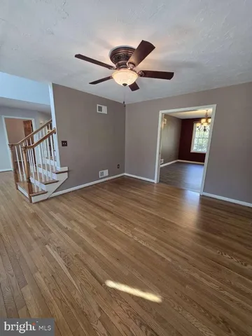 a view of an empty room with wooden floor and a ceiling fan