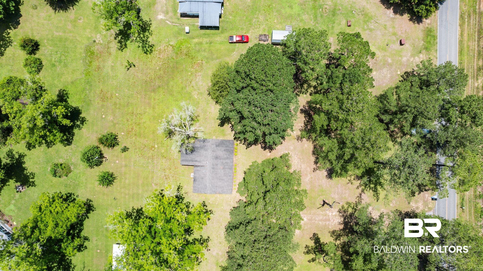 20540 Lacey Road Silverhill, AL 36576 - Photo 37 of 40 Expansive rural property featuring a primary residence with a dark-toned roof, substantial surrounding green space, mature trees providing natural shading, and a paved road bordering the property