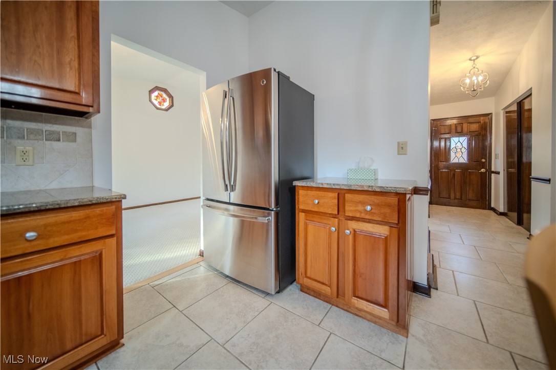 698 Albert Horning Road Atwater, OH 44201 - Photo 26 of 40 Kitchen featuring brown cabinets, freestanding refrigerator, decorative backsplash, light stone countertops, and light tile patterned floors
