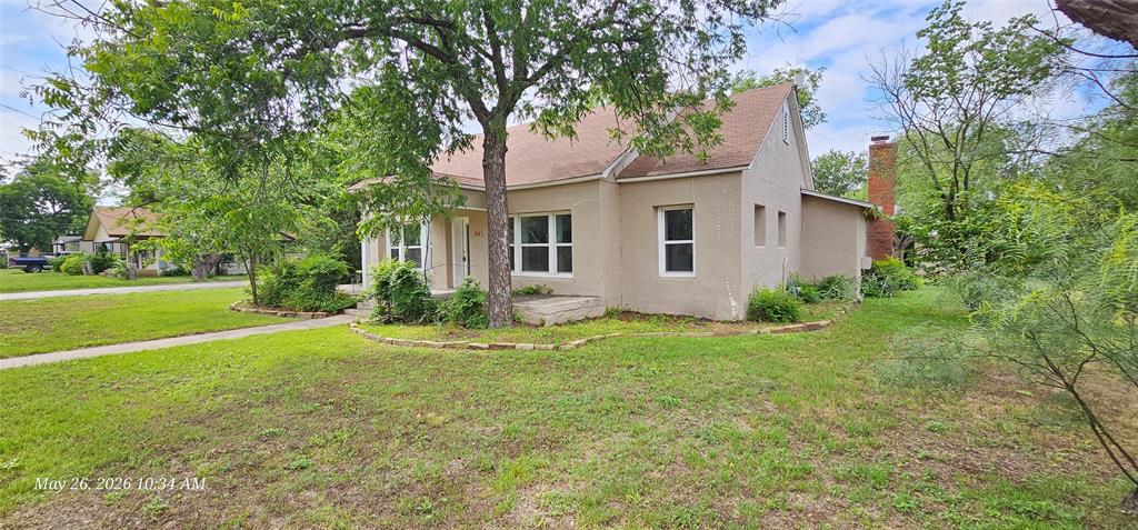 616 East 9th Street Coleman, TX 76834 - Photo 3 of 30 Exterior stucco residence featuring a sloped roof, multiple windows with white trim, a visible chimney, and an established tree