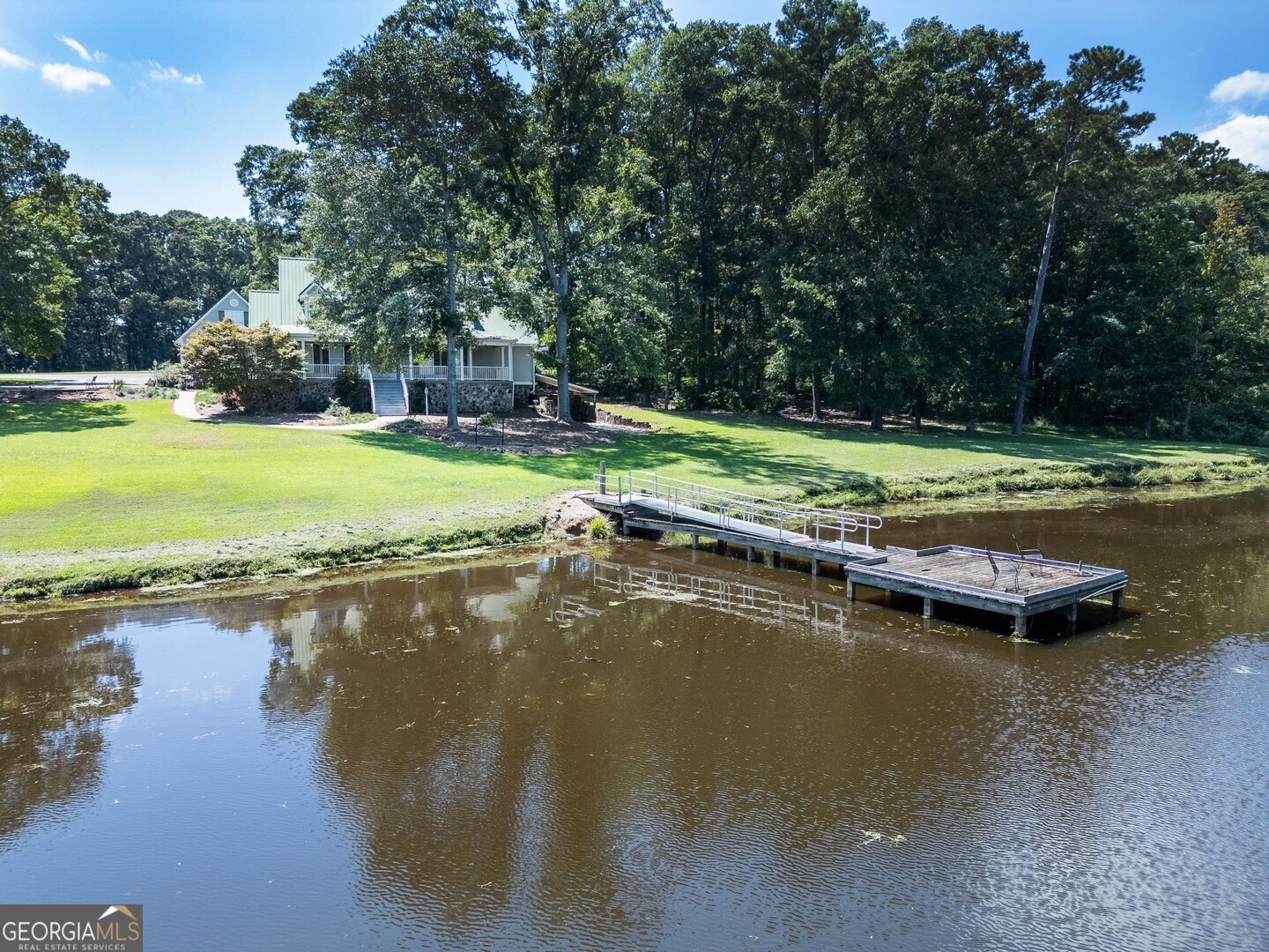 a view of a lake with lawn chairs and large trees