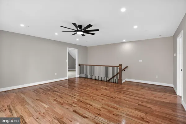 a view of an empty room with wooden floor and a ceiling fan