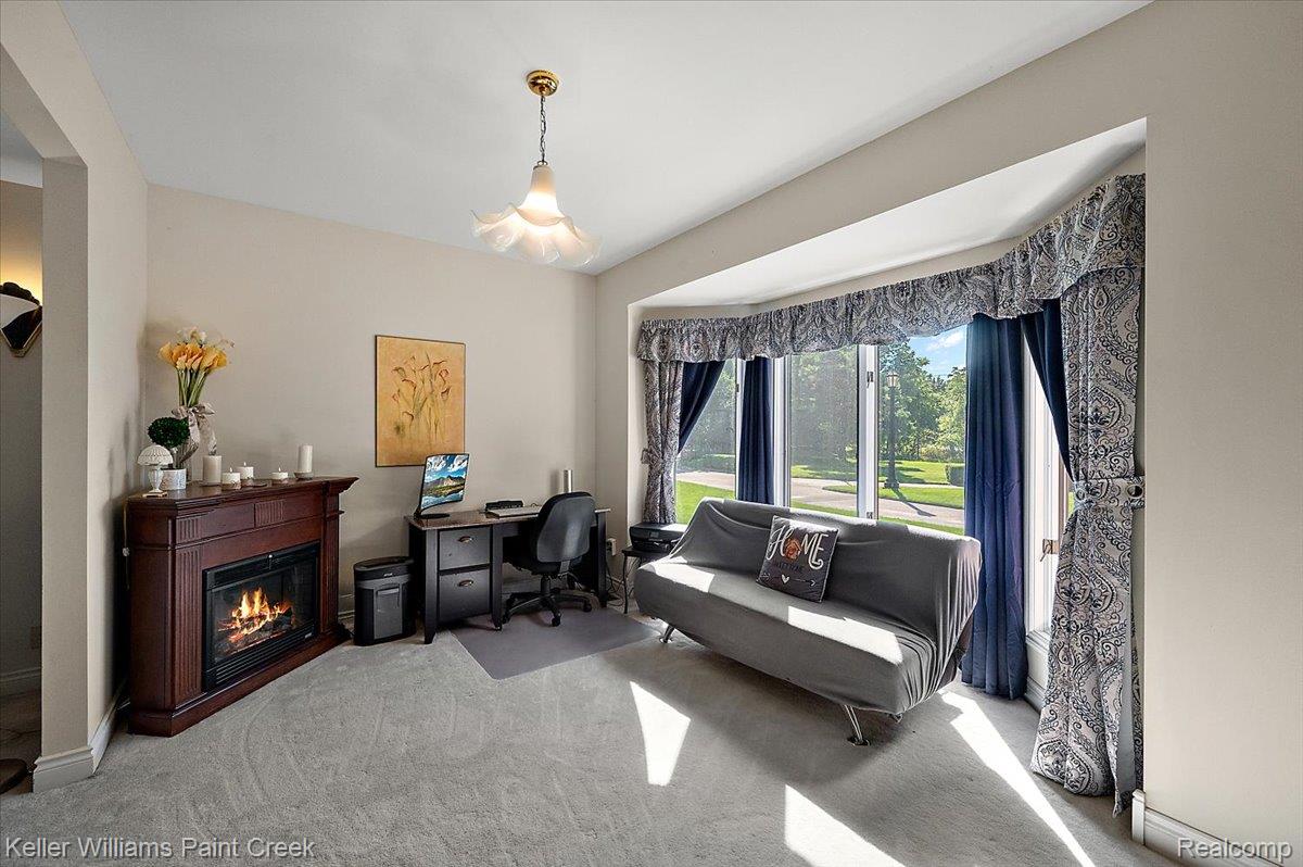 69069 Campground Road Romeo, MI 48065 - Photo 40 of 78 Inviting room featuring a corner-set fireplace with a wood-finish mantel, light-colored carpeting, a bright bay window, and a central decorative pendant light fixture