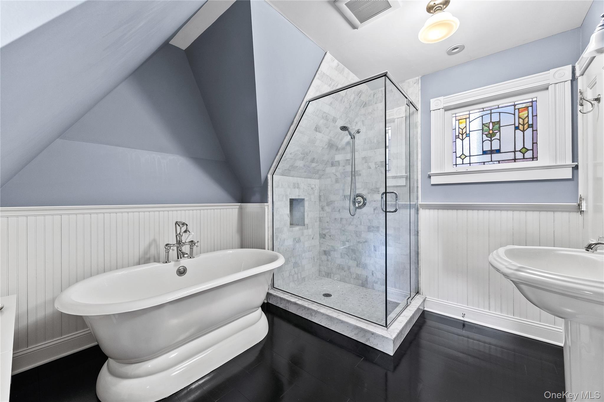 19 Howe Place Bronxville, NY 10708 - Photo 23 of 37 Bathroom featuring a freestanding bathtub, glass-enclosed shower with tiled surround, pedestal sink, dark wood-finish flooring, and a decorative stained-glass window