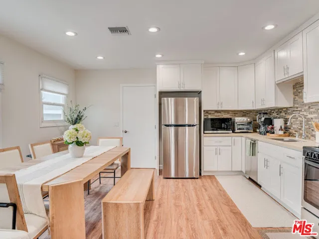 a kitchen with stainless steel appliances granite countertop a refrigerator a sink dishwasher a stove and white cabinets with wooden floor