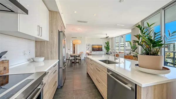 a large white kitchen with stainless steel appliances a sink a counter top space and living room view