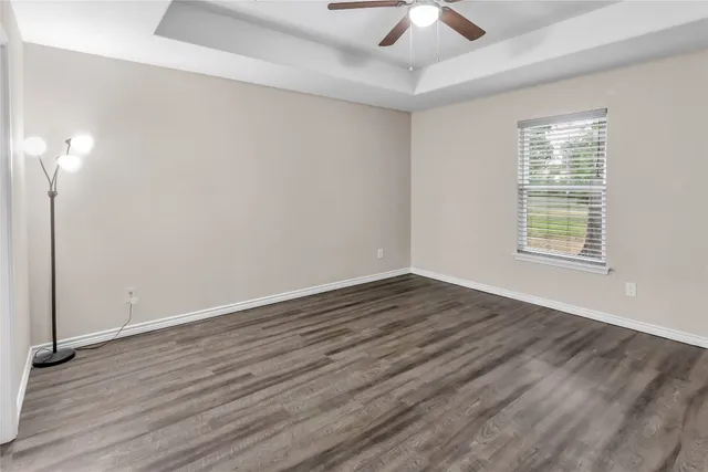 an empty room with wooden floor chandelier fan and windows