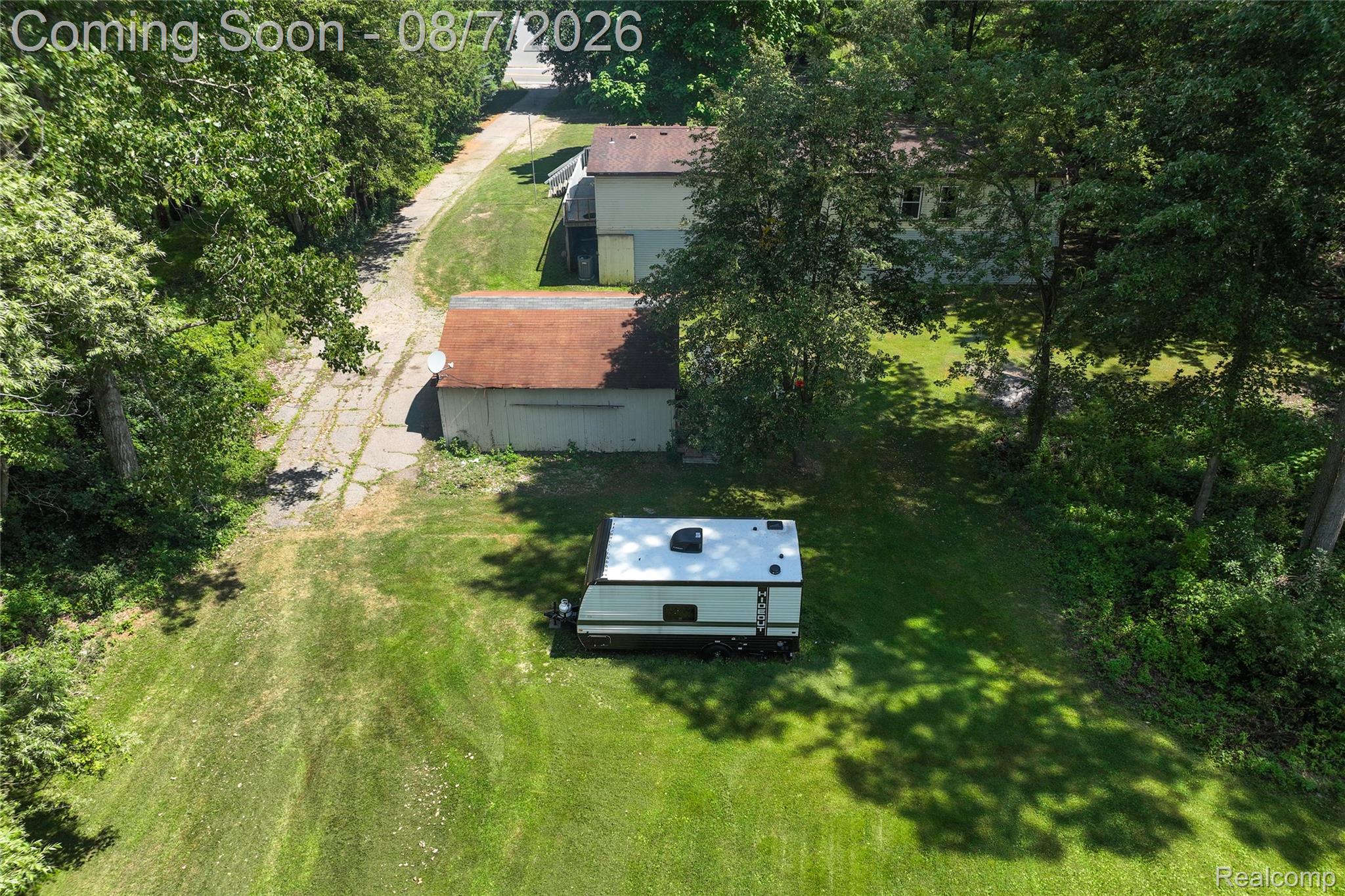 9940 Bunton Road Willis, MI 48191 - Photo 5 of 26 Expansive green lawn with mature perimeter trees, featuring a paved driveway, a detached garage structure, and a multi-level dwelling