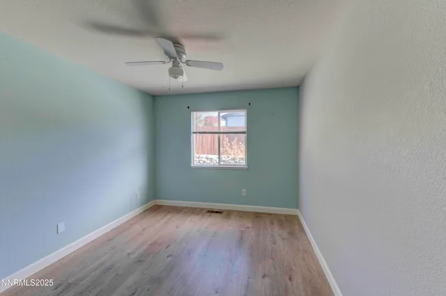 an empty room with wooden floor ceiling fan and windows