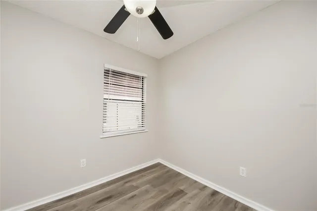an empty room with wooden floor ceiling fan and windows