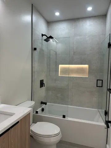 a bathroom with a granite countertop bathtub shower sink vanity and toilet