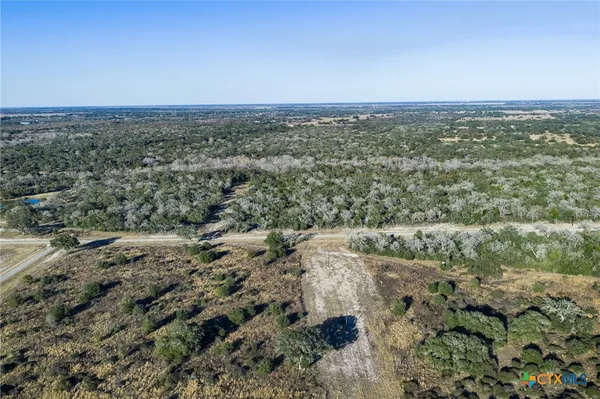 a view of a dry yard with trees in back