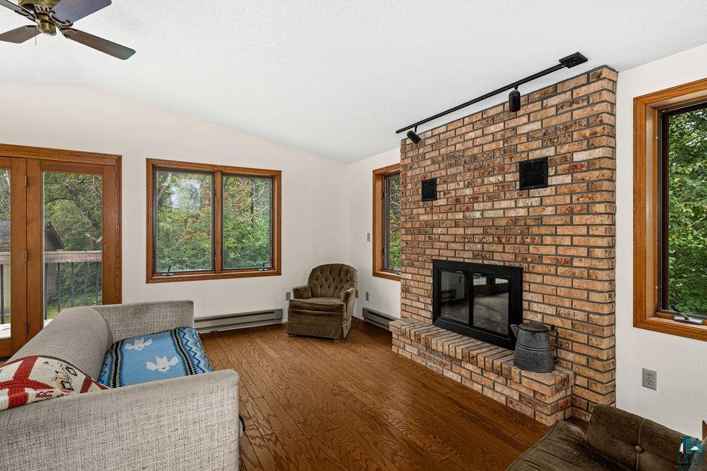 4738 Morris Thomas Road Hermantown, MN 55811 - Photo 10 of 19 Vaulted ceiling with ceiling fan, brick fireplace with hearth, wood-finish flooring, and multiple windows with wood trim