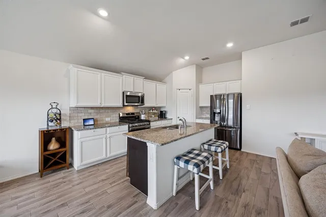 a kitchen with stainless steel appliances a stove a sink a refrigerator and chairs